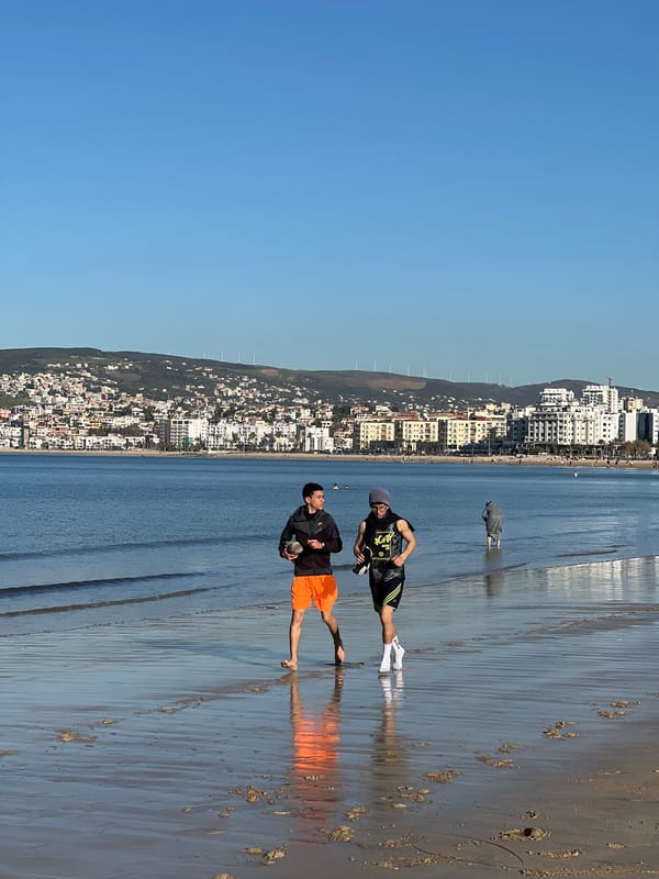 Two men pose on wet beach sand in Tangier