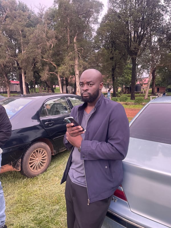 Casual hangout by parked cars on a grassy patch in Jos
