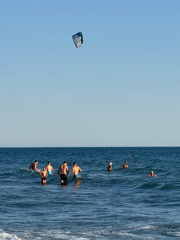 Sunny beach day with kitesurfers offshore and crowds on the sand