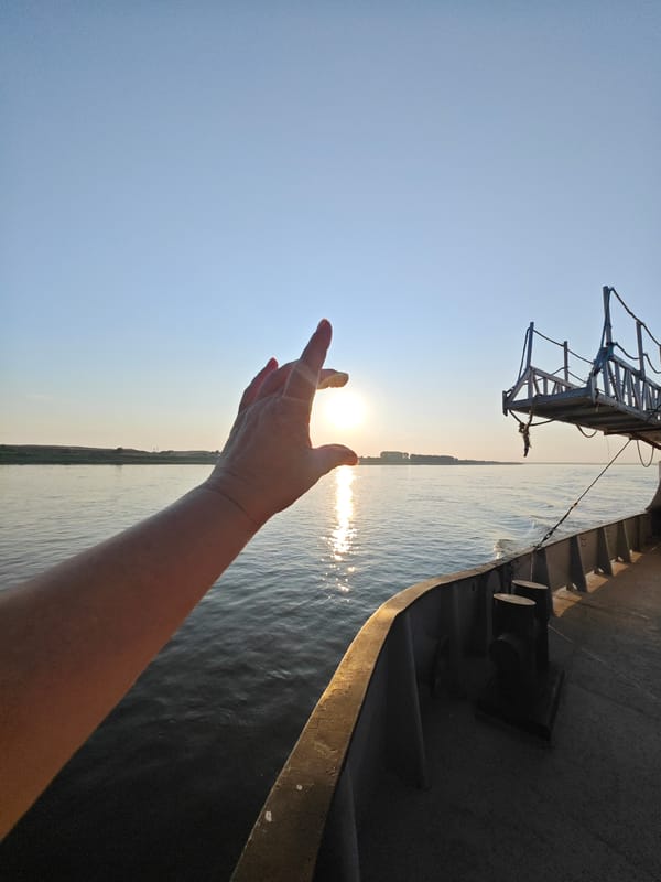 Hand reaching toward a river sunset from a ship deck