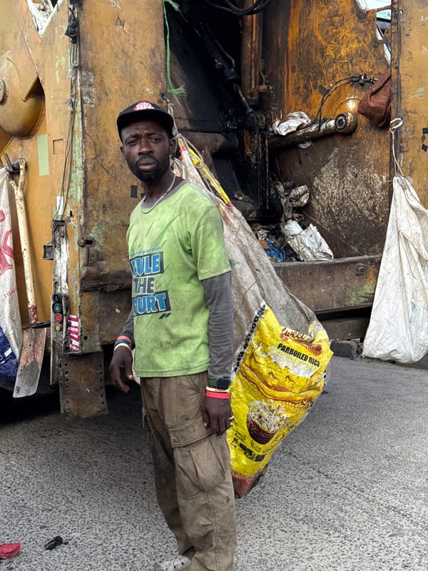 Man stands beside garbage truck during collection in Ado