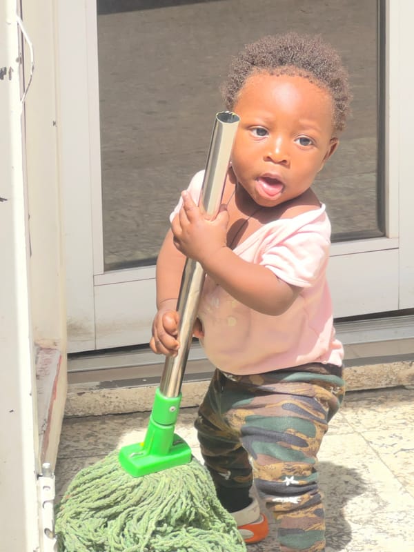 Toddler plays with mop, poses playfully in Gura Top