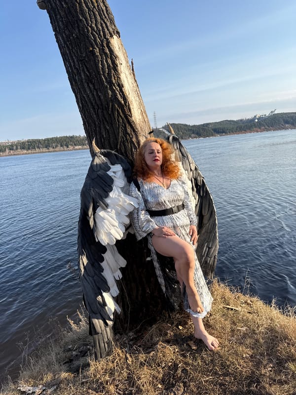 Winged costumed woman photographed on fallen tree near Russian waterfront