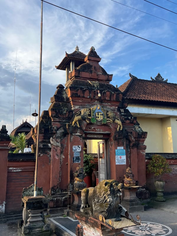 Scooter rider captured smiling past ornate gates in Singapadu