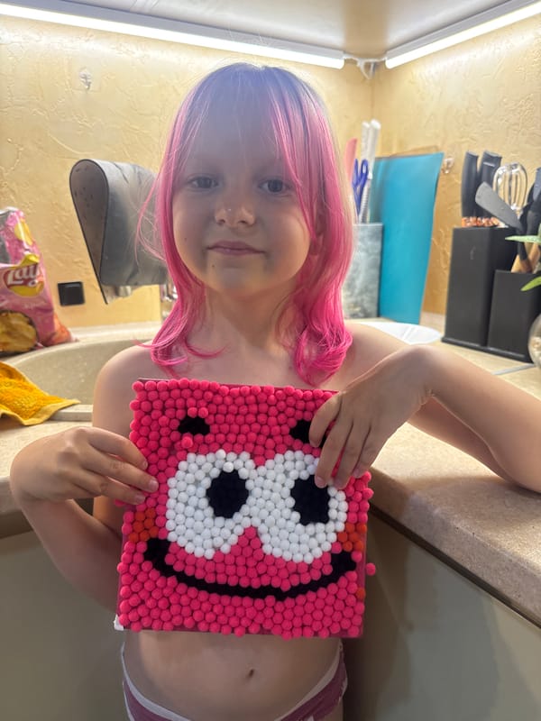 Child displays handmade pom-pom craft with face design
