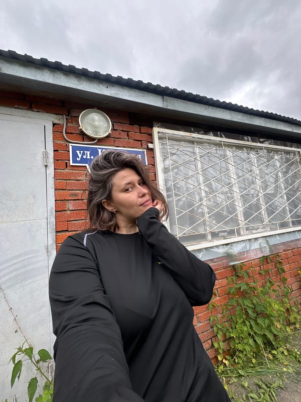 Woman takes playful selfies with plants near brick building