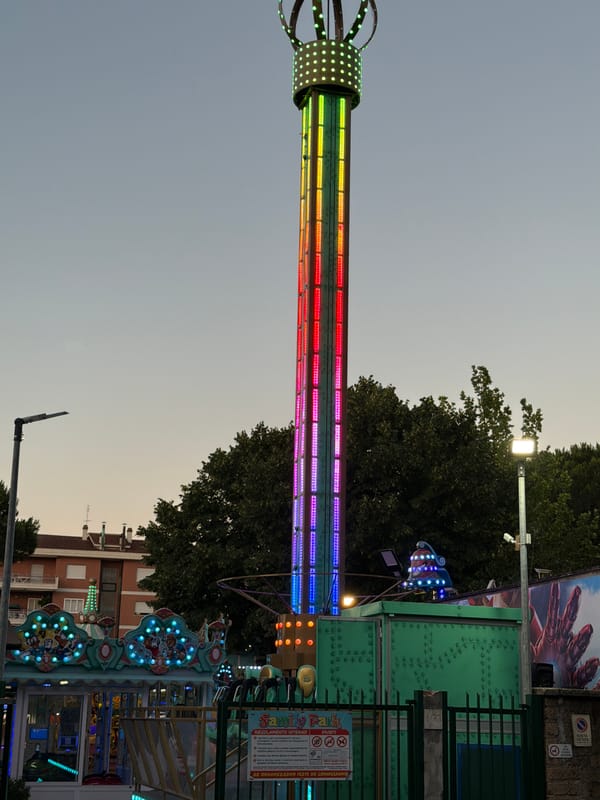 Drop tower ride glows with colorful LEDs at dusk in Rome