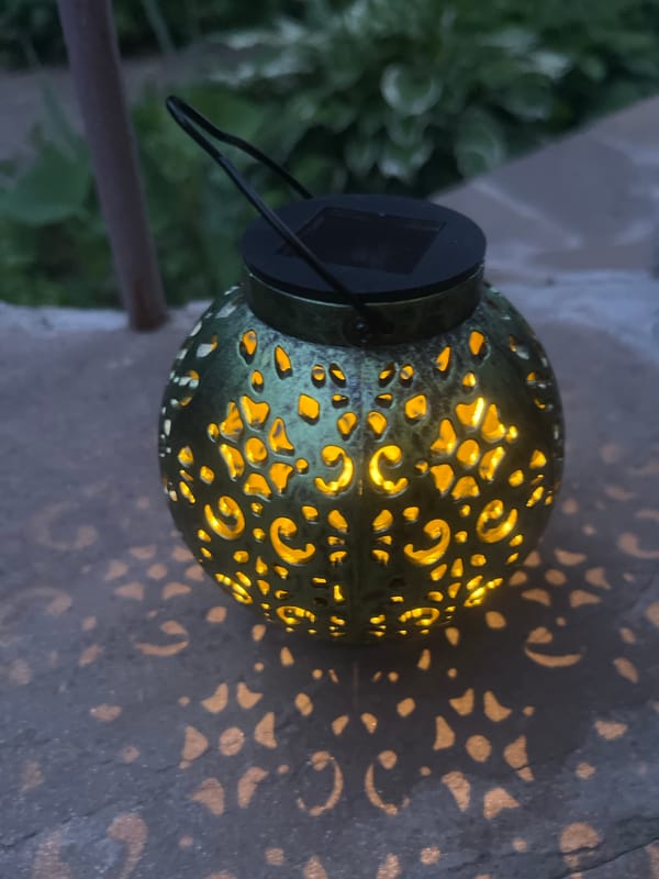 Ornate solar lantern casts patterned light on stone at dusk