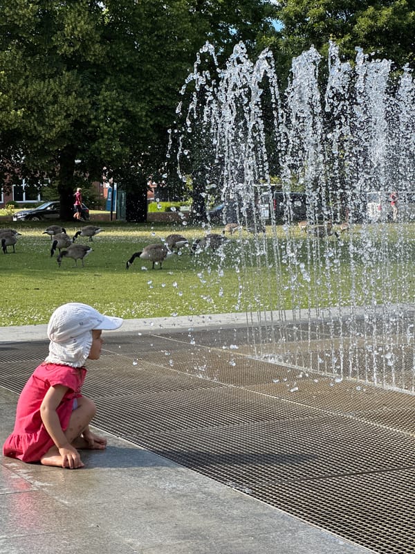 Kids cool off at a Kiel park fountain on a sunny afternoon