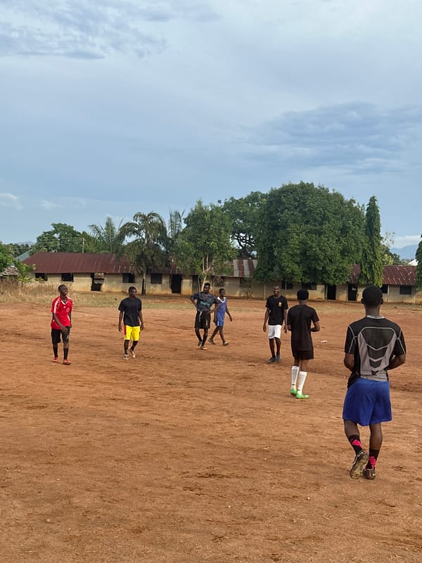 Seven young men gather outdoors on dirt surface