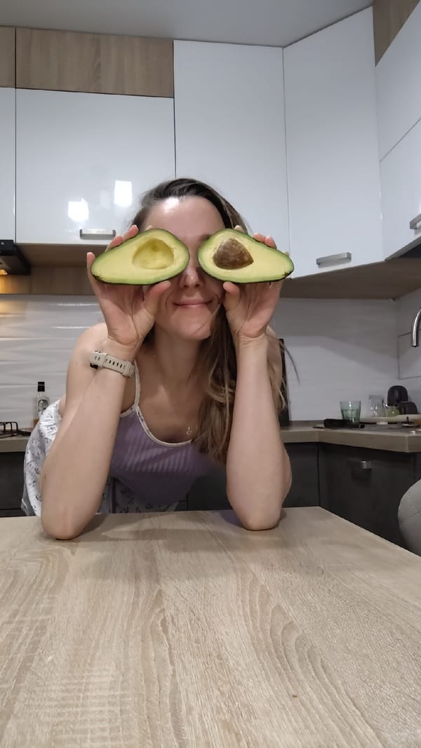 Woman poses playfully with avocado halves in kitchen