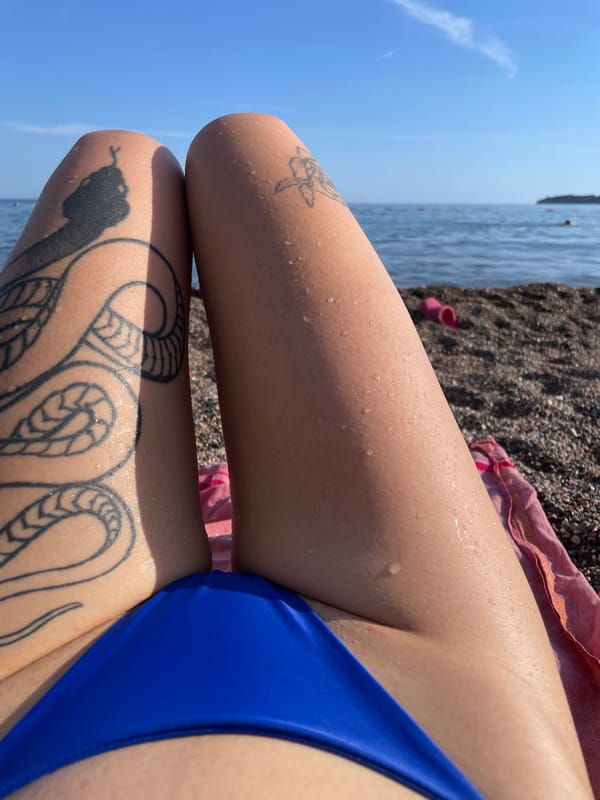 Tattooed woman sunbathes on Montenegro beach amid spring blooms