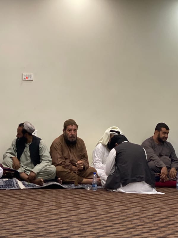 Five people seated on carpet inside a Kandahar interior space