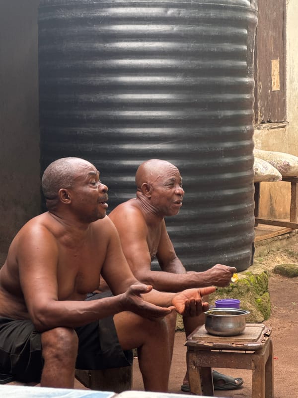 Two men photographed sitting outside in Aboh, Nigeria