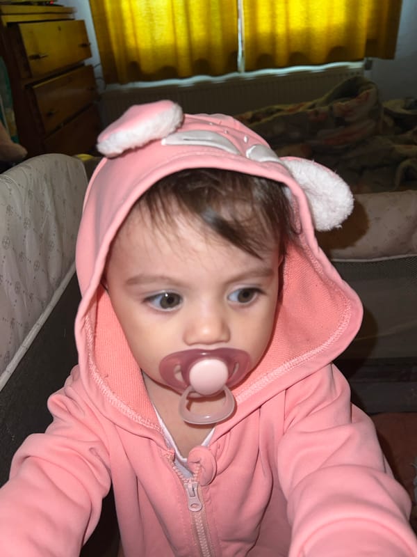 Baby in pink hooded outfit rests peacefully in Elena crib