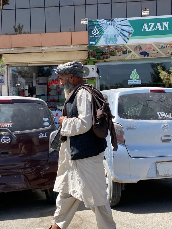 Man in traditional dress walks Kandahar street carrying bundle
