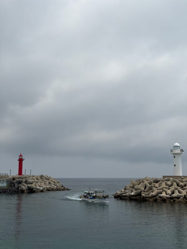 Fishing boat passes through twin-lighthouse harbor entrance in Jeju