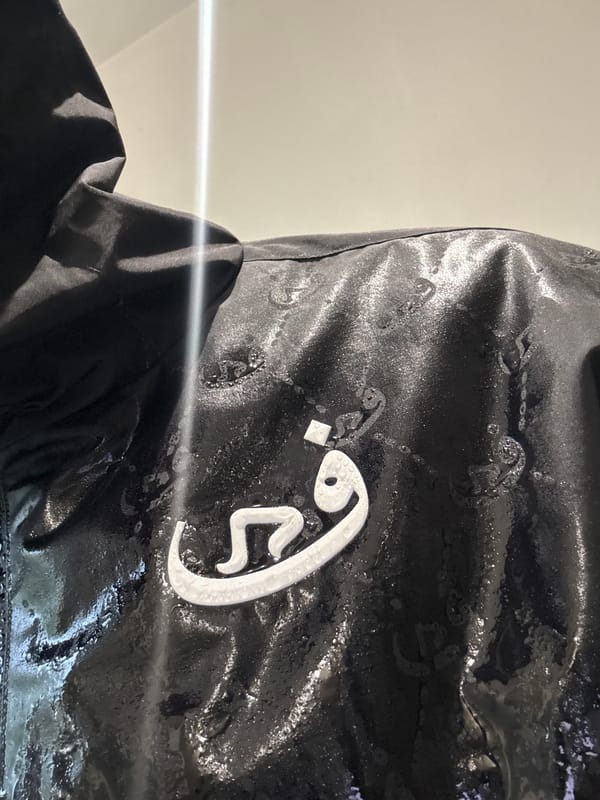 Person photographed with Arabic-lettered garment and iPhone in Massy