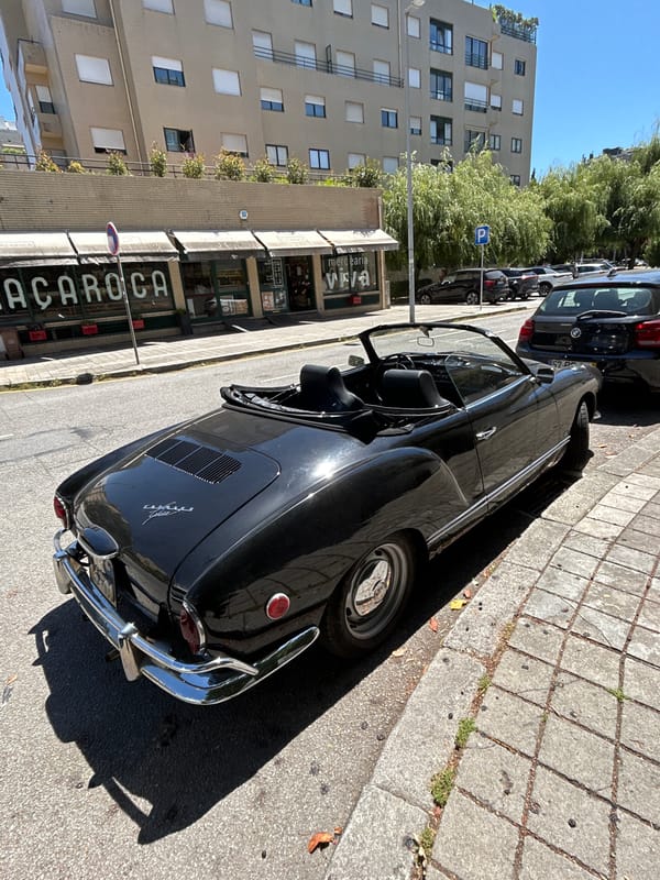 Black Karmann Ghia convertible parked on a city street, top down.
