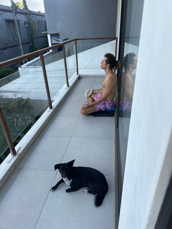Man meditates on balcony with dog in Mengwi