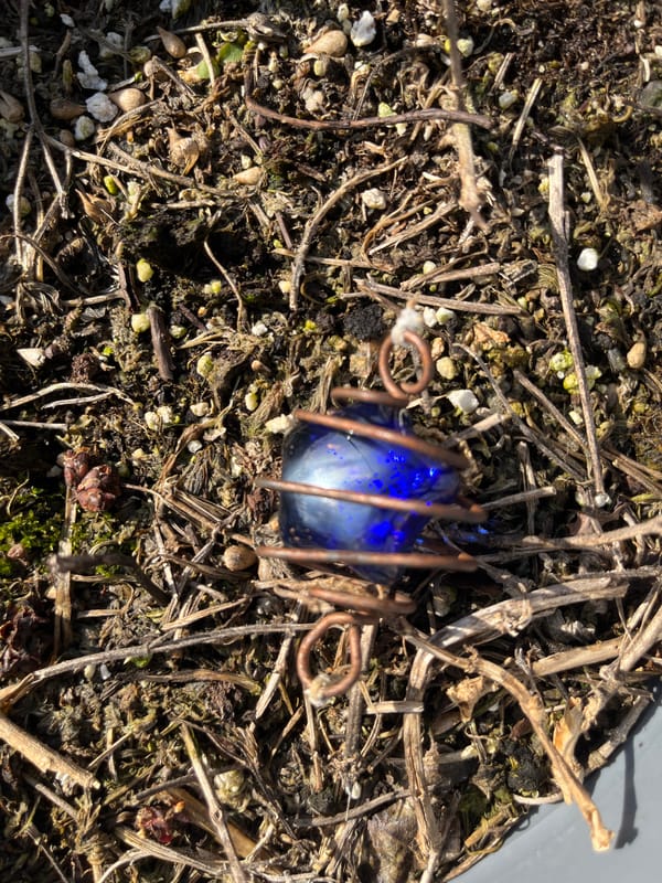 Blue glass object in copper wire found on plant debris