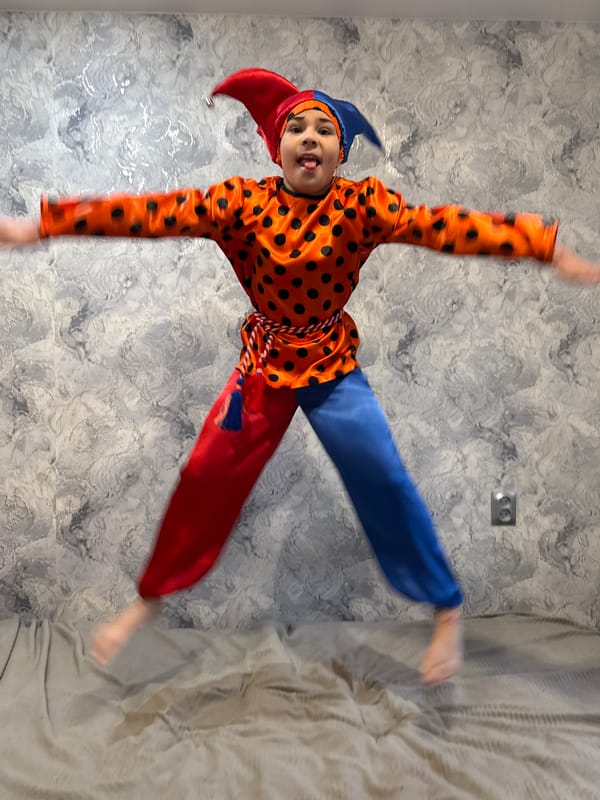 Child plays in jester costume, jumps on bed