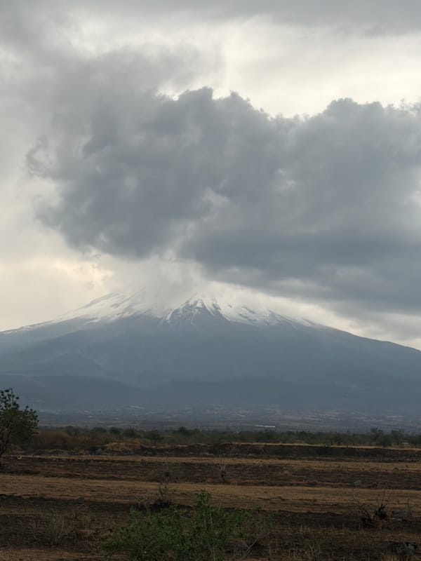 Snow-covered Popocatépetl volcano visible through clouds over Metepec
