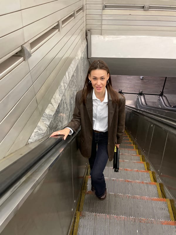 Woman rides escalator in Saint Petersburg wearing brown jacket