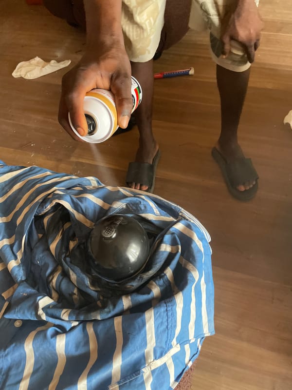 Person spray paints object on wooden floor in Ojomu