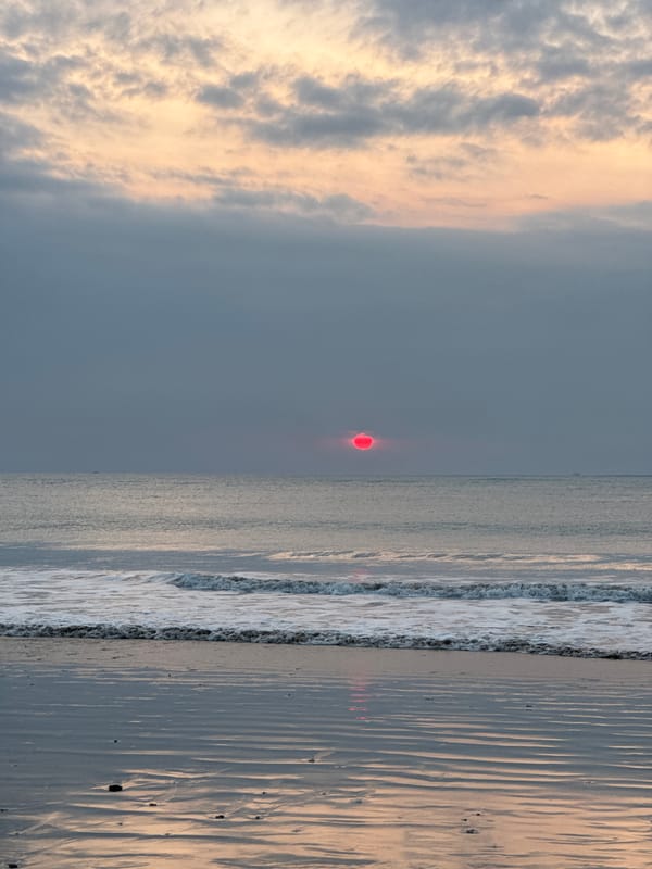 Red sun setting over Kuta Selatan beach, people at the shoreline