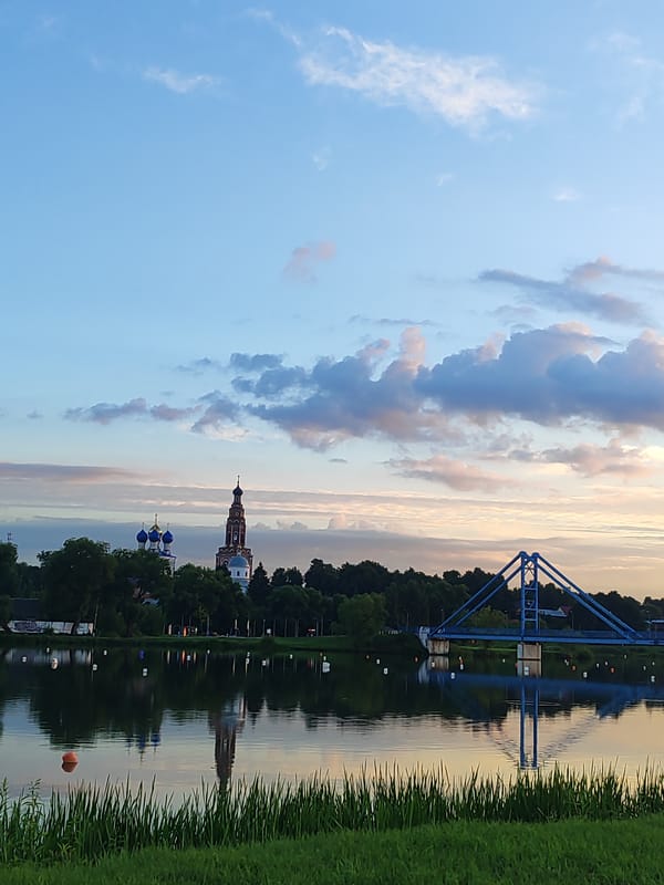 Blue pedestrian bridge over calm water at dusk, Bronnitsy