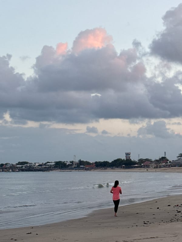 Kuta Beach at dusk: walkers, fishers, dogs, and dramatic clouds.