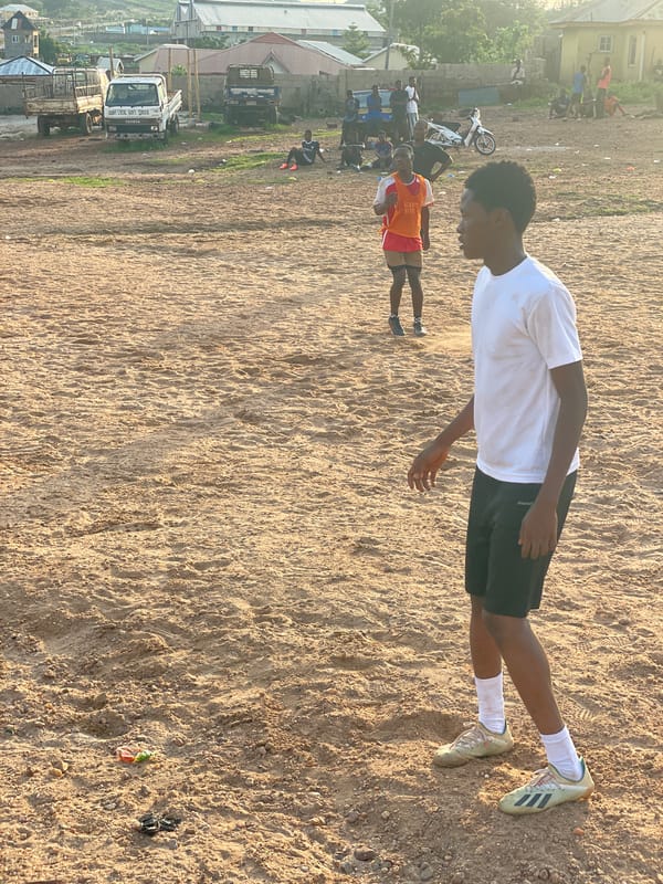 Pickup football on a sandy Lokoja field, late afternoon.