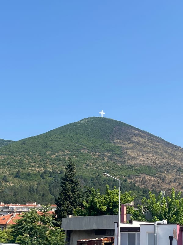 Mountain cross, river bridge, and book monument in a European town