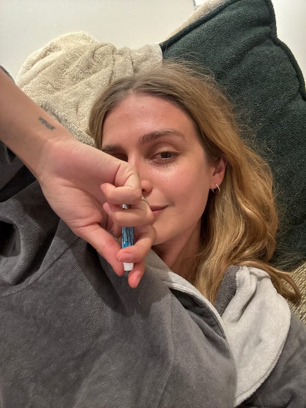 Person in grey robe rests on cushions holding tube