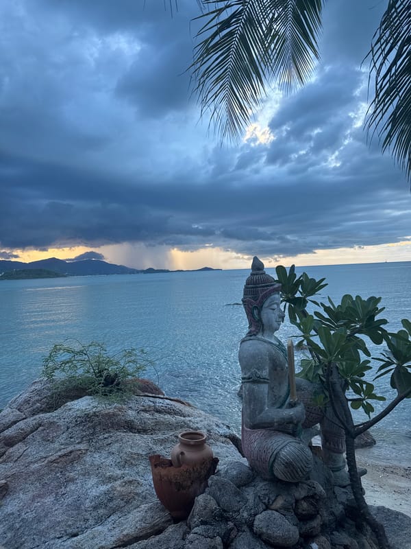 Ko Samui at dusk: coastal statue, stormy sunset, warm lamp indoors