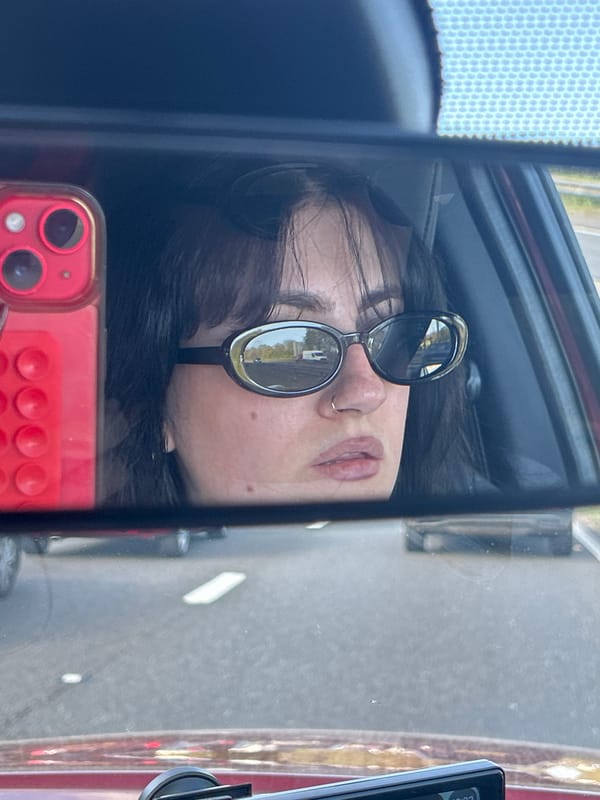 Person with red phone reflected in car window