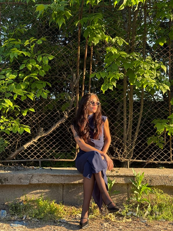 Woman rests on ledge near overgrown fence in Pleven