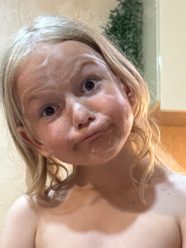 Person applies face cream, poses with palm leaf indoors