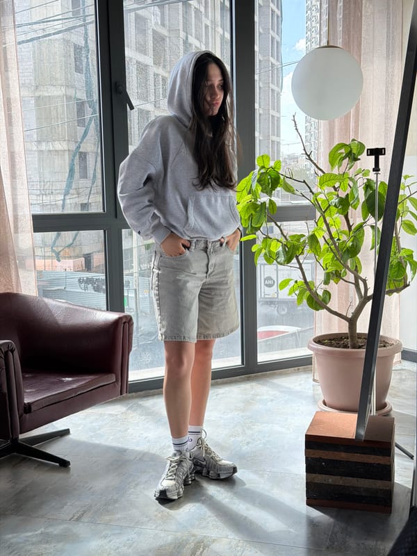 Woman in gray hoodie stands by window in Yerevan
