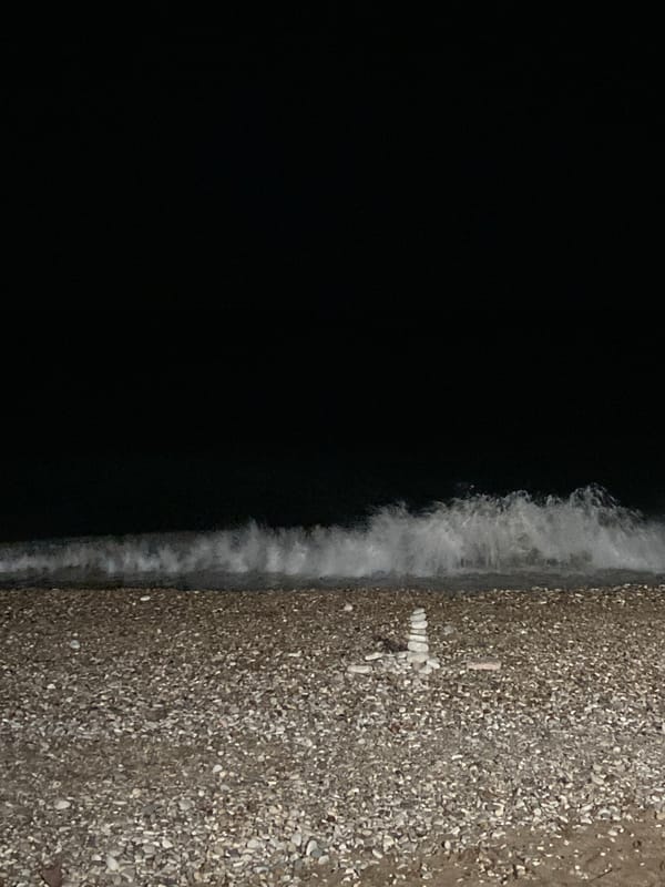 Nighttime waves wash pebble beach with stone cross in Bar