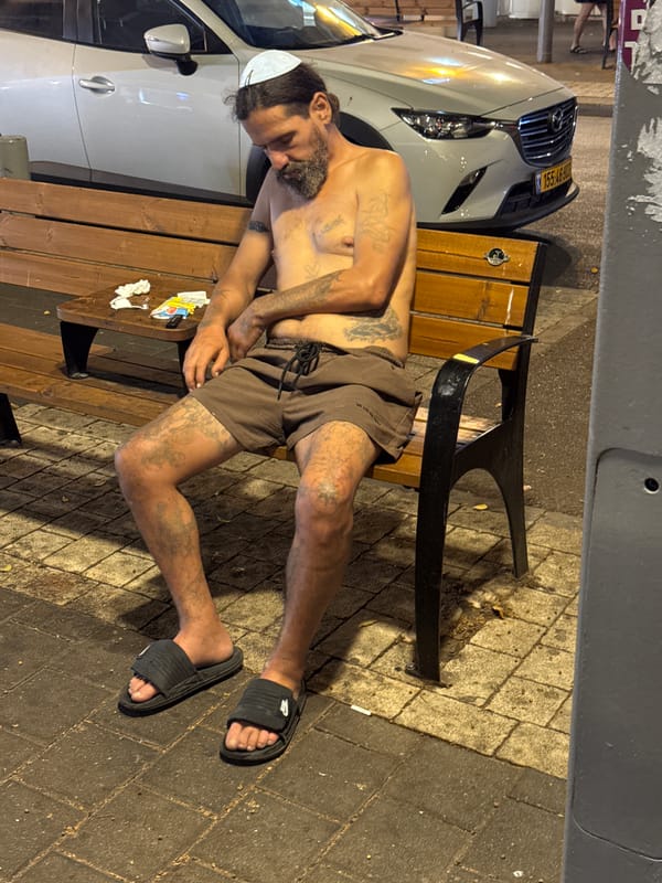 Resting on a Tel Aviv bench at night, kippah and tattoos