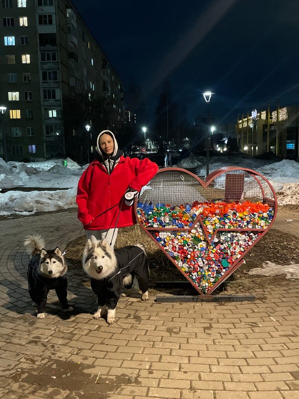 Woman with dogs poses by heart-shaped bottle cap recycling container