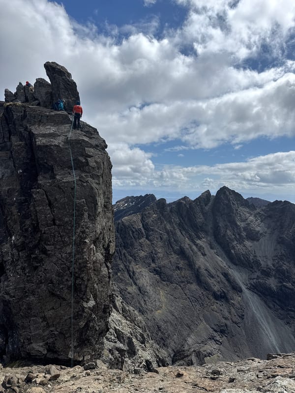 Three climbers scale jagged cliff in mountainous region