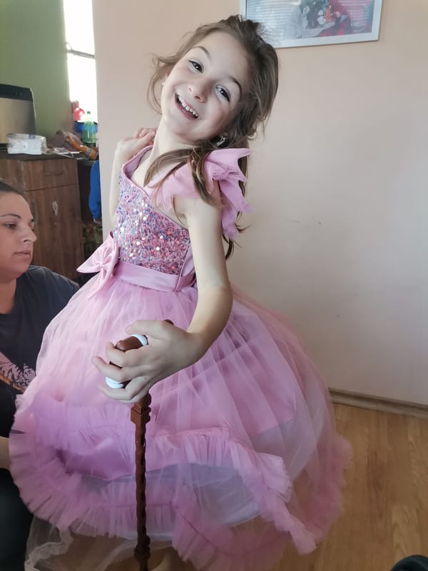 Girl in pink dress uses walking cane indoors