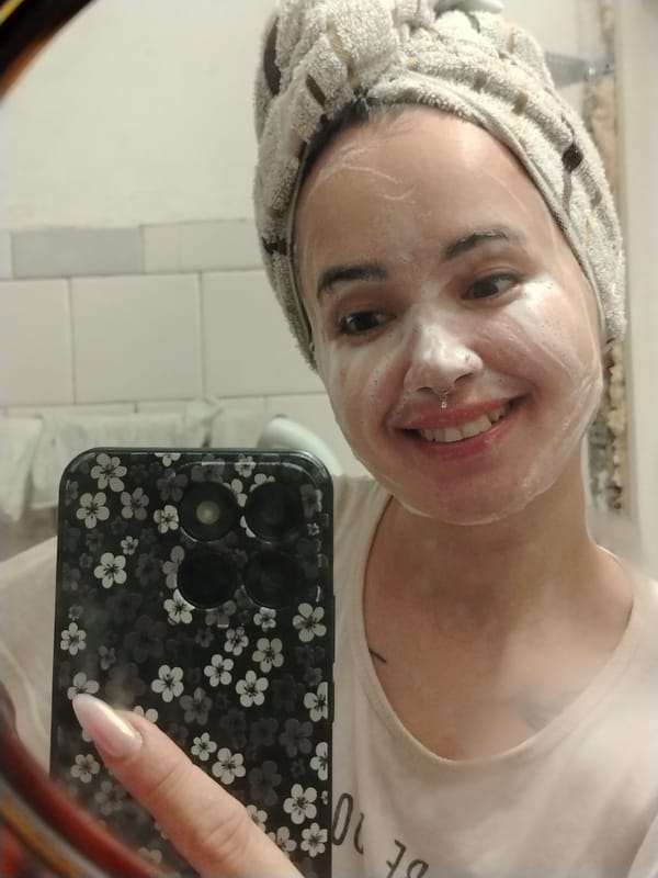 Mirror selfie mid-cleanse, foam on face and towel on head.