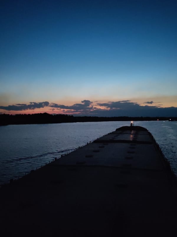 Nighttime waterway scenes show barge and illuminated cable-stayed bridge
