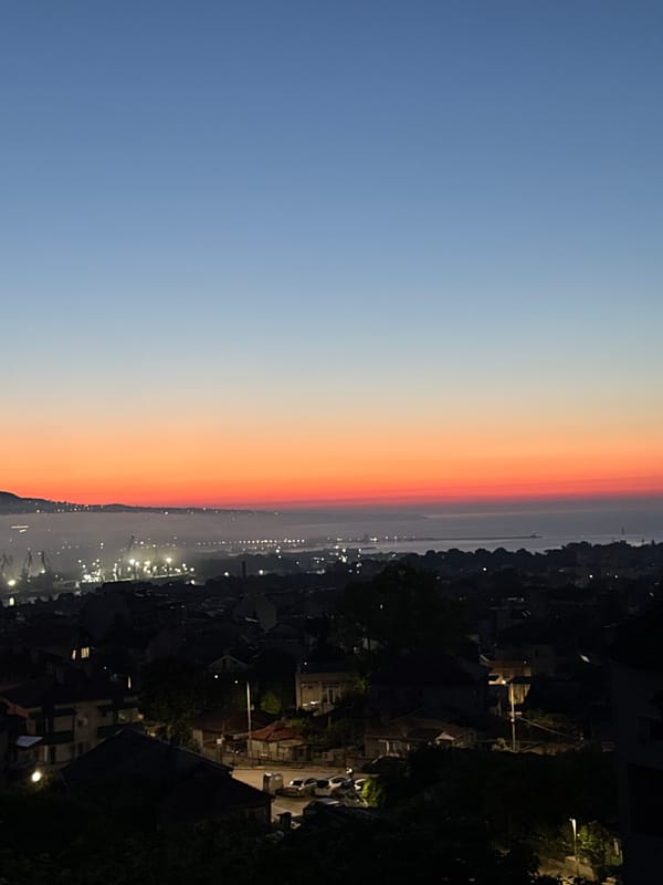 City skyline photographed during colorful twilight with crescent moon visible