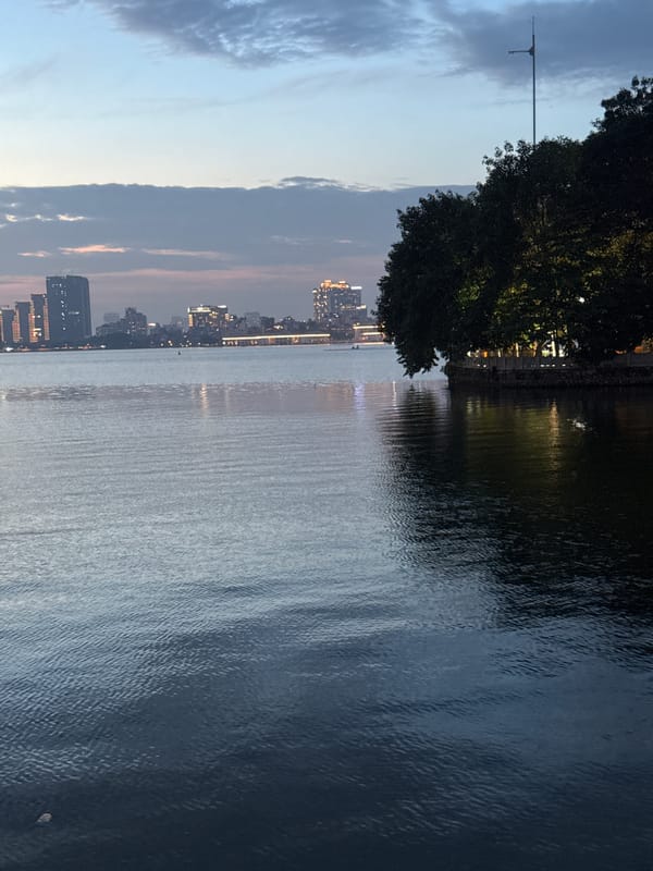 Dusk at West Lake waterfront, Hanoi — people, signs, and skyline