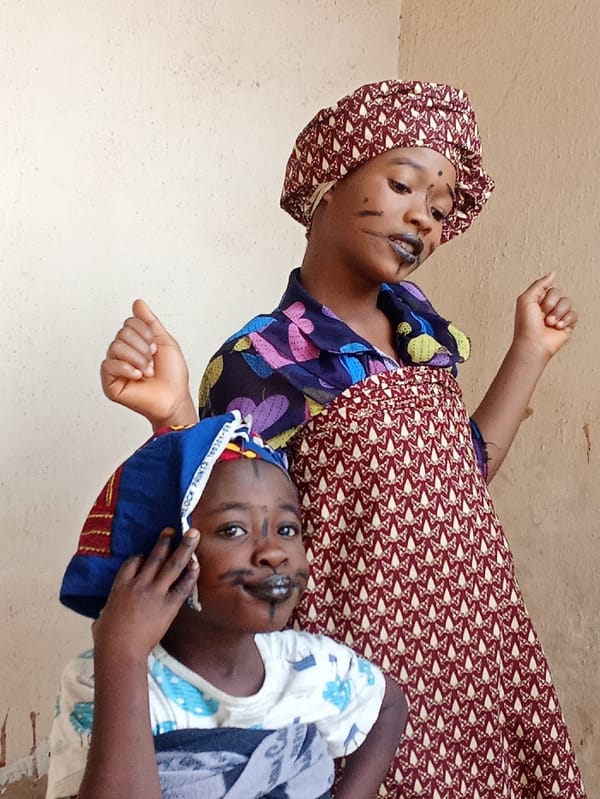 Children play dress-up while adults repair motorcycles in Akwanga